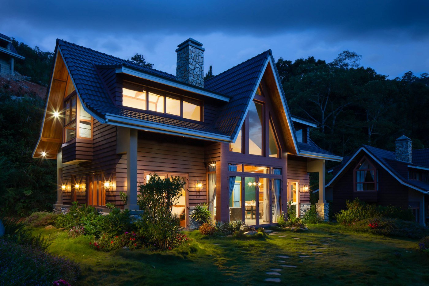 A timber house at dusk with a stone chimney and warm light in the windows