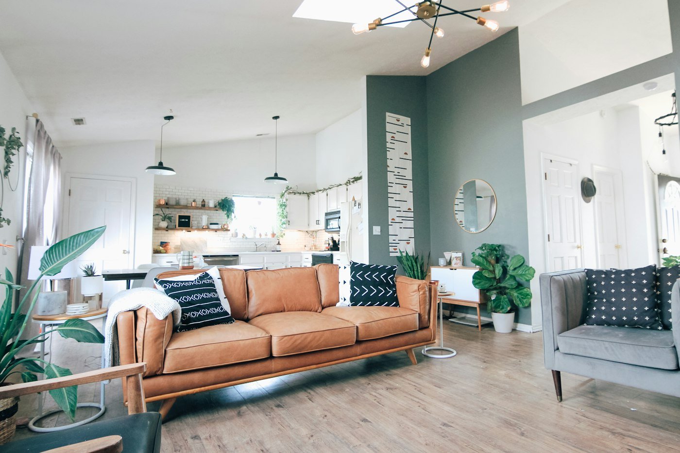 A tan leather sofa, a grey armchair, and a kitchen visible beyond the seating